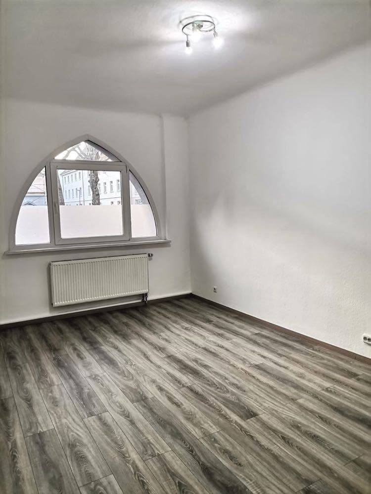 Leerer sanierter Wohnraum mit Rundbogenfenster und neuem Vinylboden in Grau